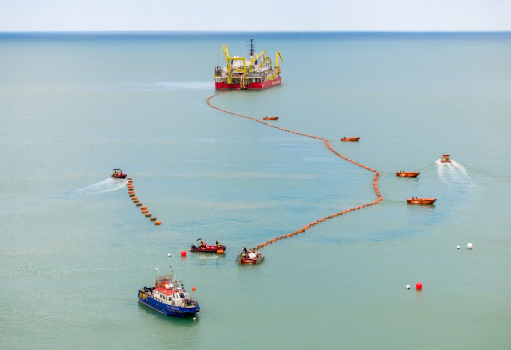 Marine operation with vessels and a large ship in the sea, featuring orange barriers.