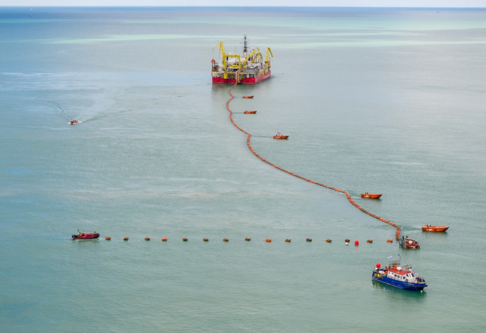 View of a large ship with orange booms and smaller boats in a calm sea
