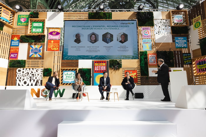 Conference at the ChangeNOW event, with four speakers discussing on stage in front of an audience, surrounded by colorful panels bearing inspirational messages.