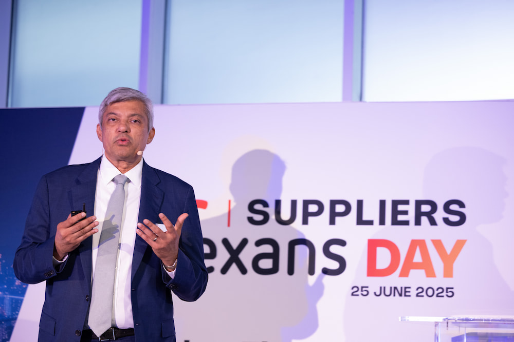 Speaker presenting at Suppliers Day event with a promotional backdrop.