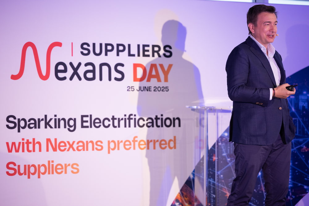 Speaker presenting at Nexans Suppliers Day event with vibrant backdrop