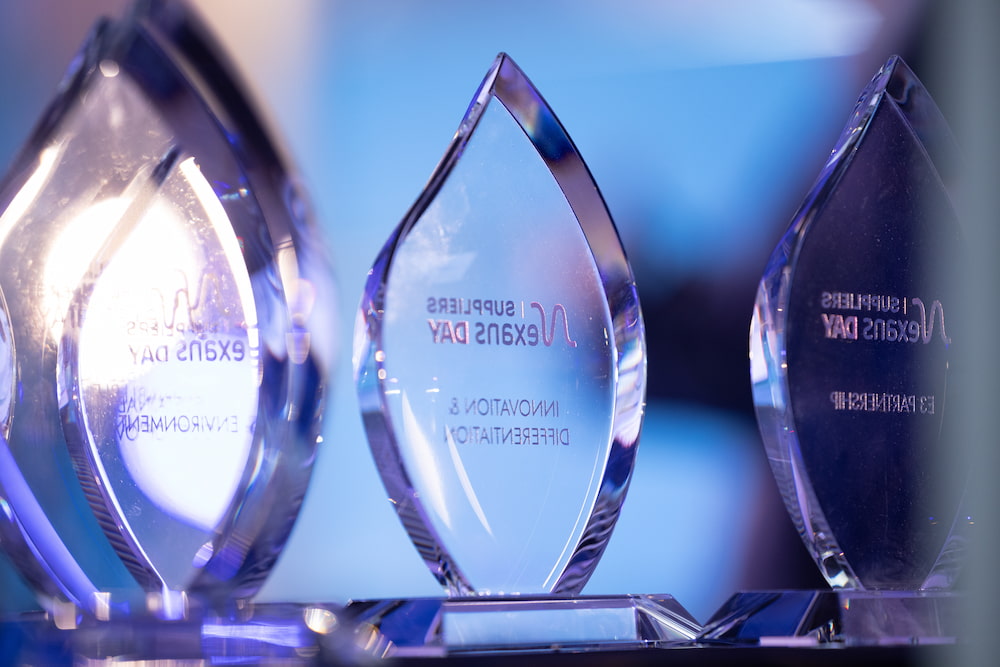 Three elegant crystal awards reflecting light from a blue background, celebrating suppliers' achievements.