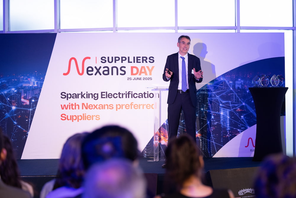 Speaker presenting at a suppliers event with visual backdrop of a city skyline and awards on stage.