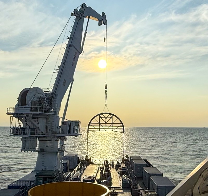 Grue de bateau levée au-dessus de l'océan au coucher de soleil, avec structure suspendue.